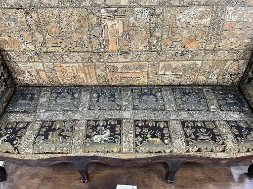 A sofa with embroidered upholstery. The back half of the seat is dusty and the front half is clean.