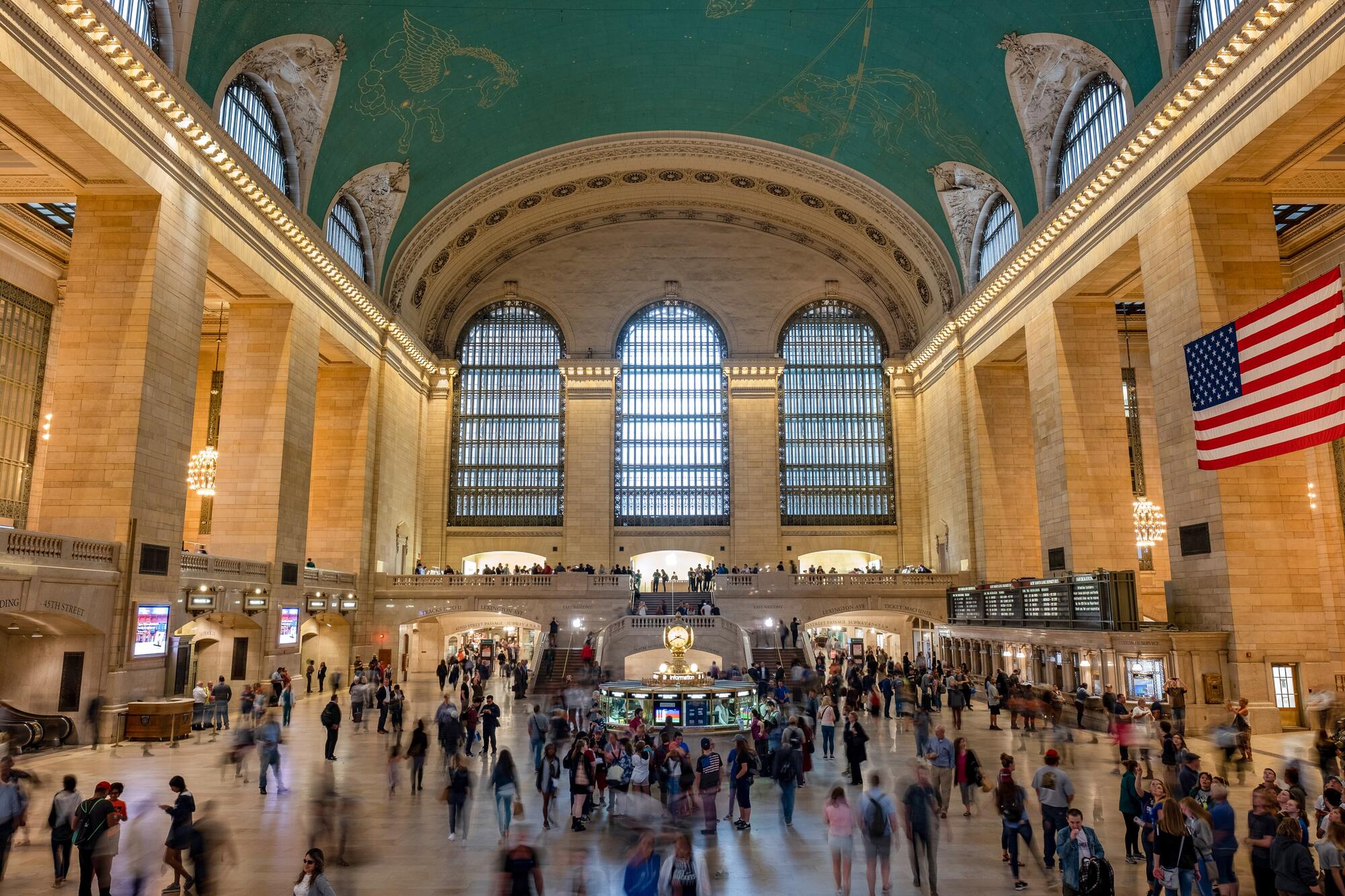 A large train station concourse with a blue ceiling painted with stars and constellations.