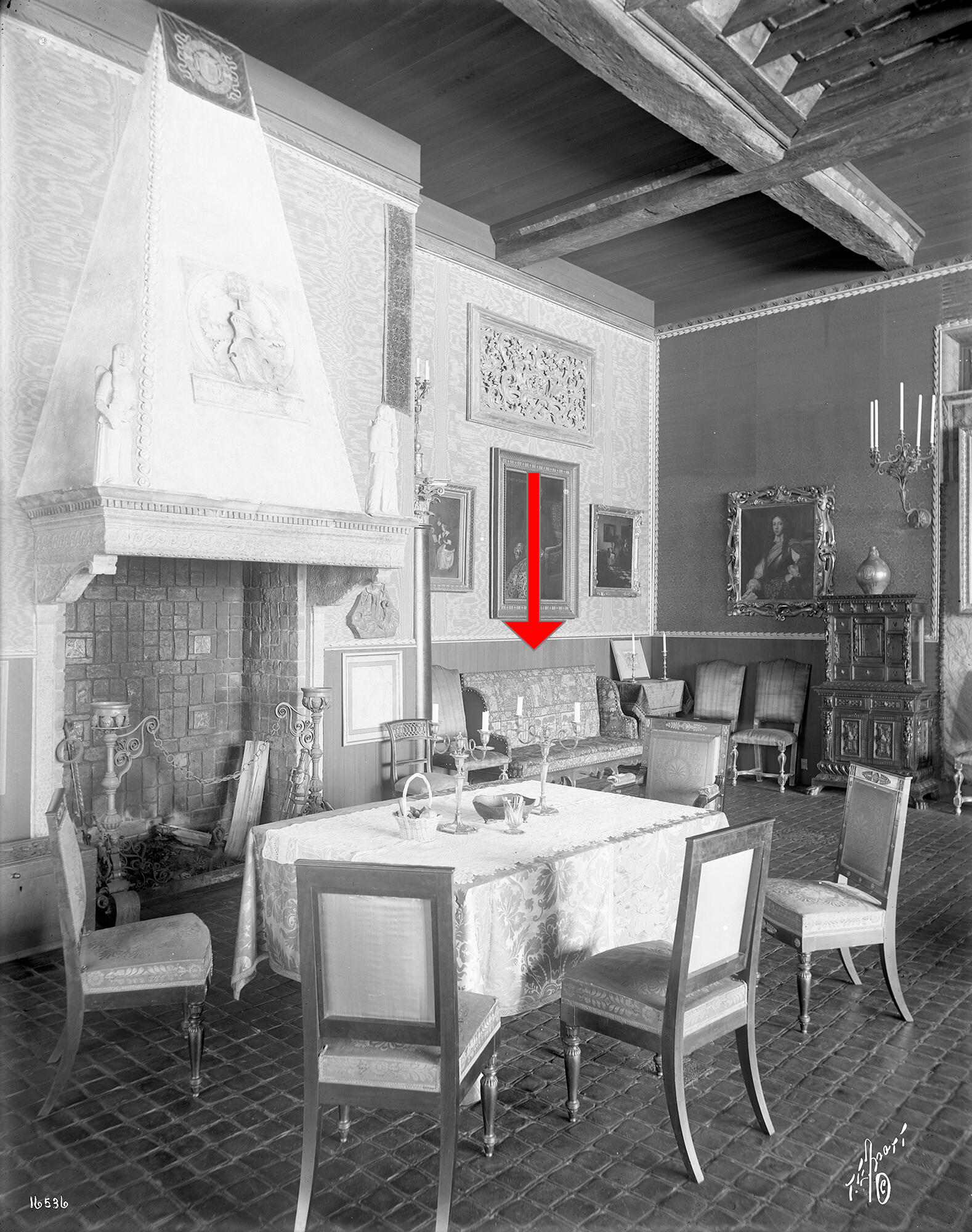 A black and white photograph of the corner of a room with paintings and furniture with an arrow pointing to the sofa. The seat of the sofa is streamlined.