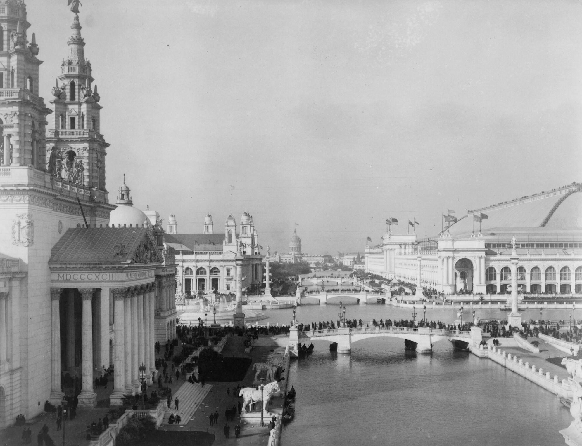 A black and white photograph of white Beaux-Arts style buildings on canals with people walking on sidewalks and over pedestrian bridges.