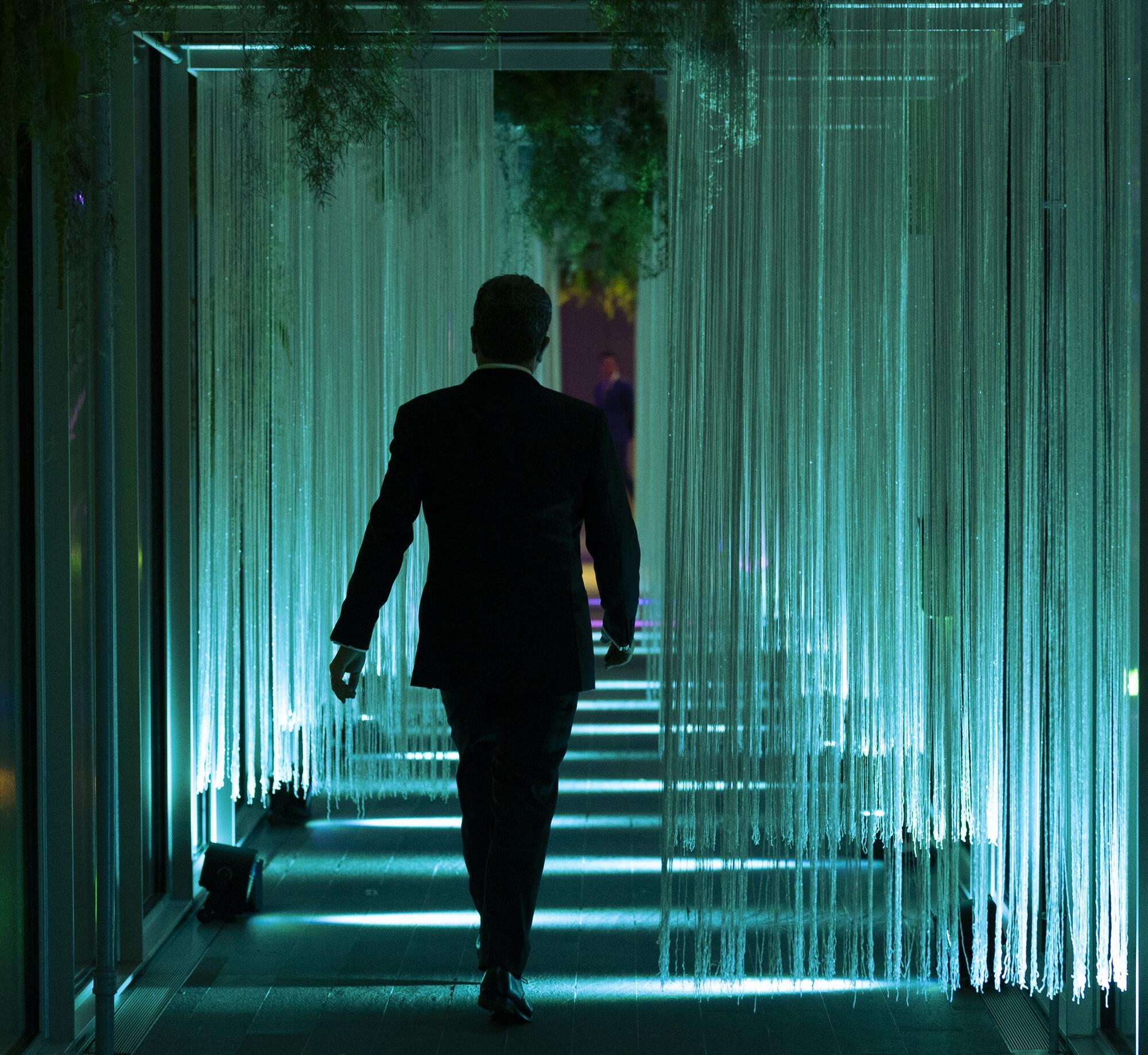 A silhouette of person walking down an illuminated hall of glowing vertical strands