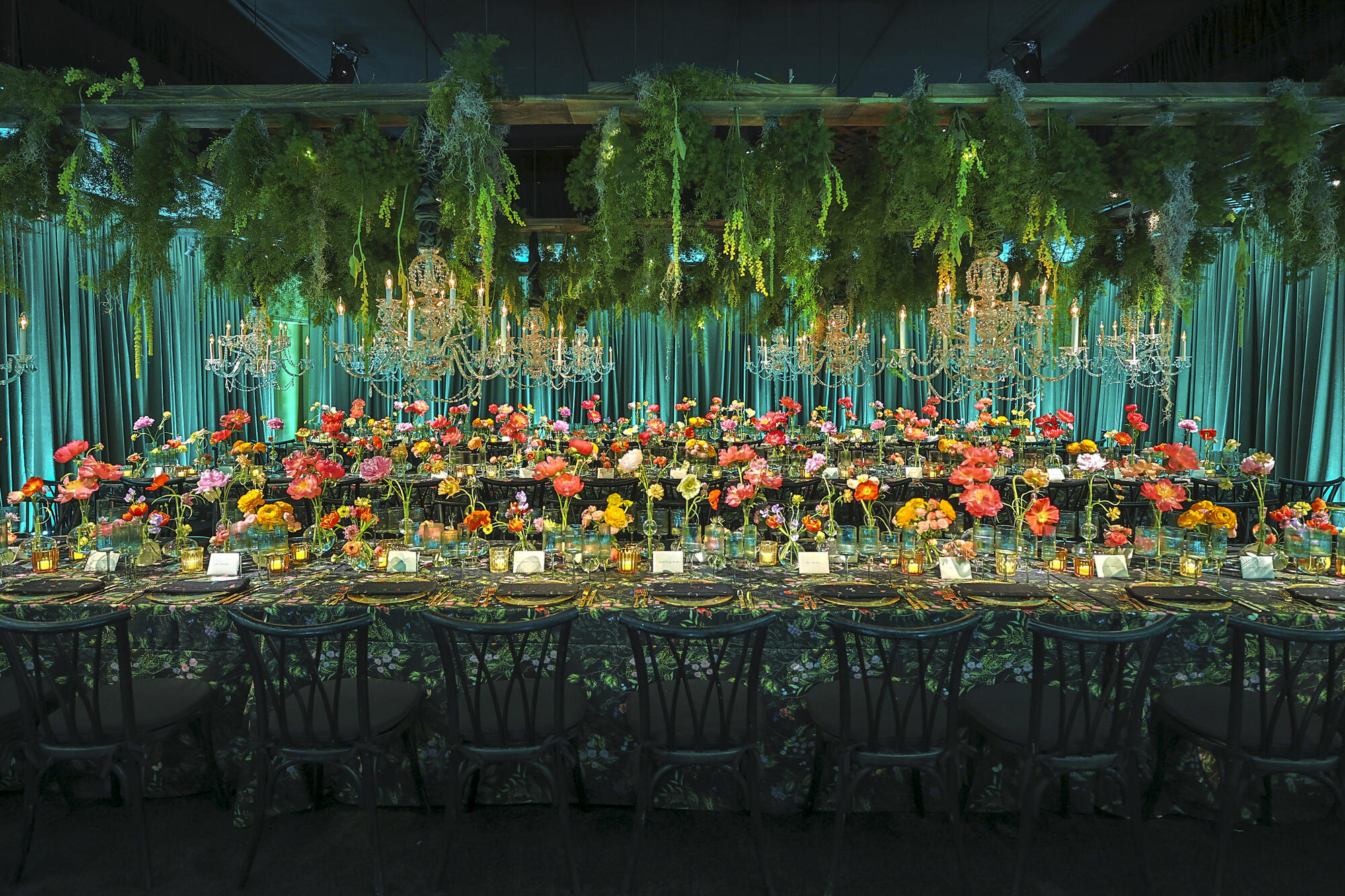 A long table decorated with flowers and dangling greenery and set for dining