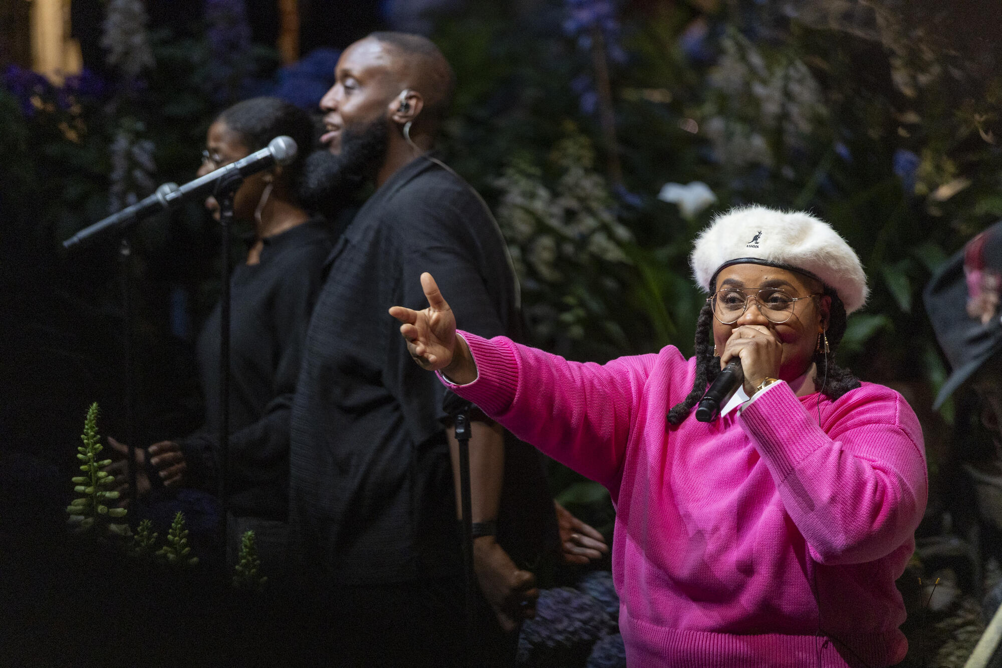A Black woman in a pink sweater and furry beret singing into a microphone