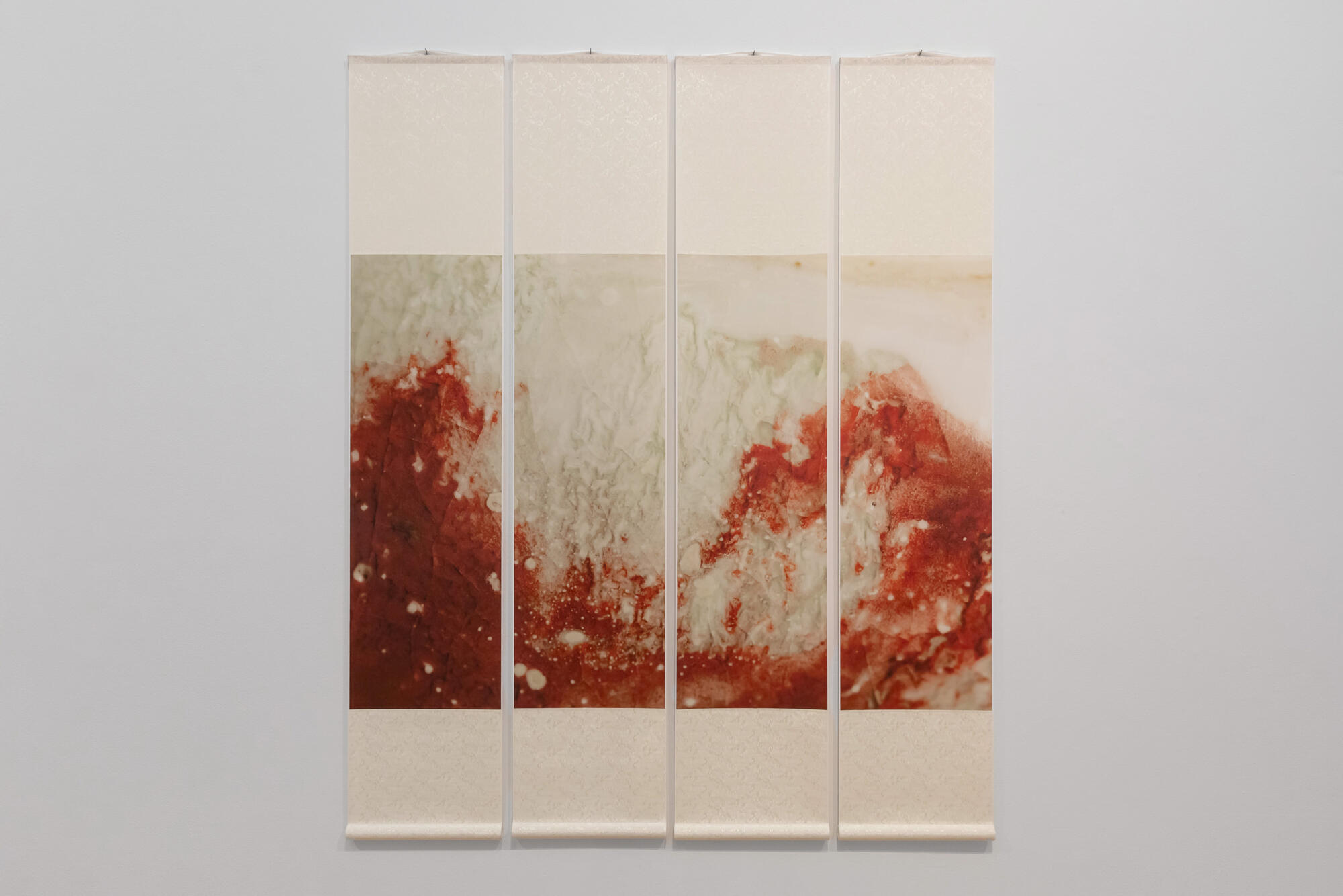 A multi-panel ink artwork in colors of red displayed on a white wall