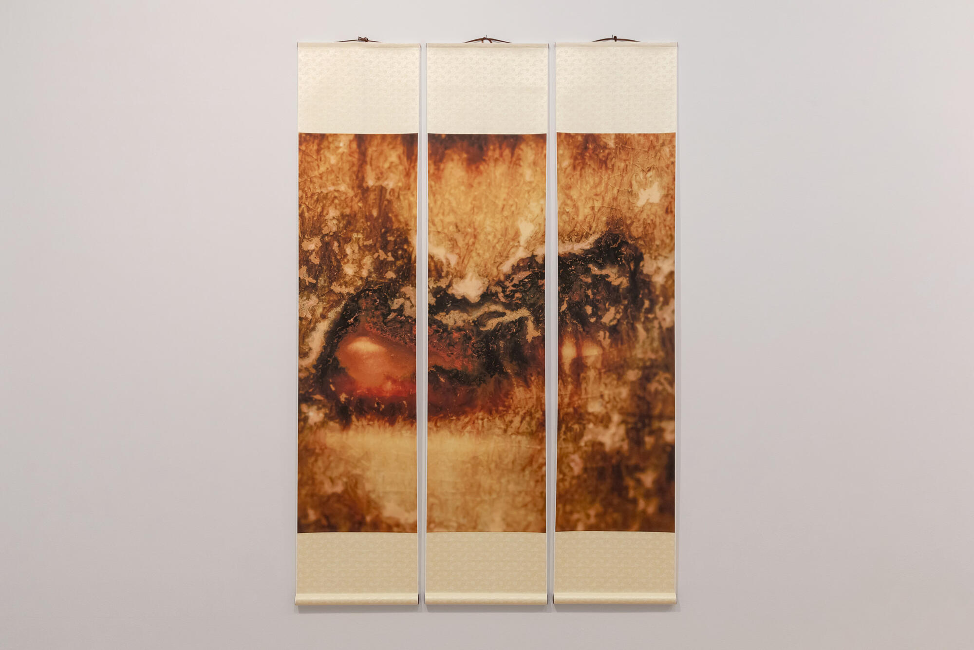 A multi-panel ink artwork in colors of orange and brown displayed on a white wall