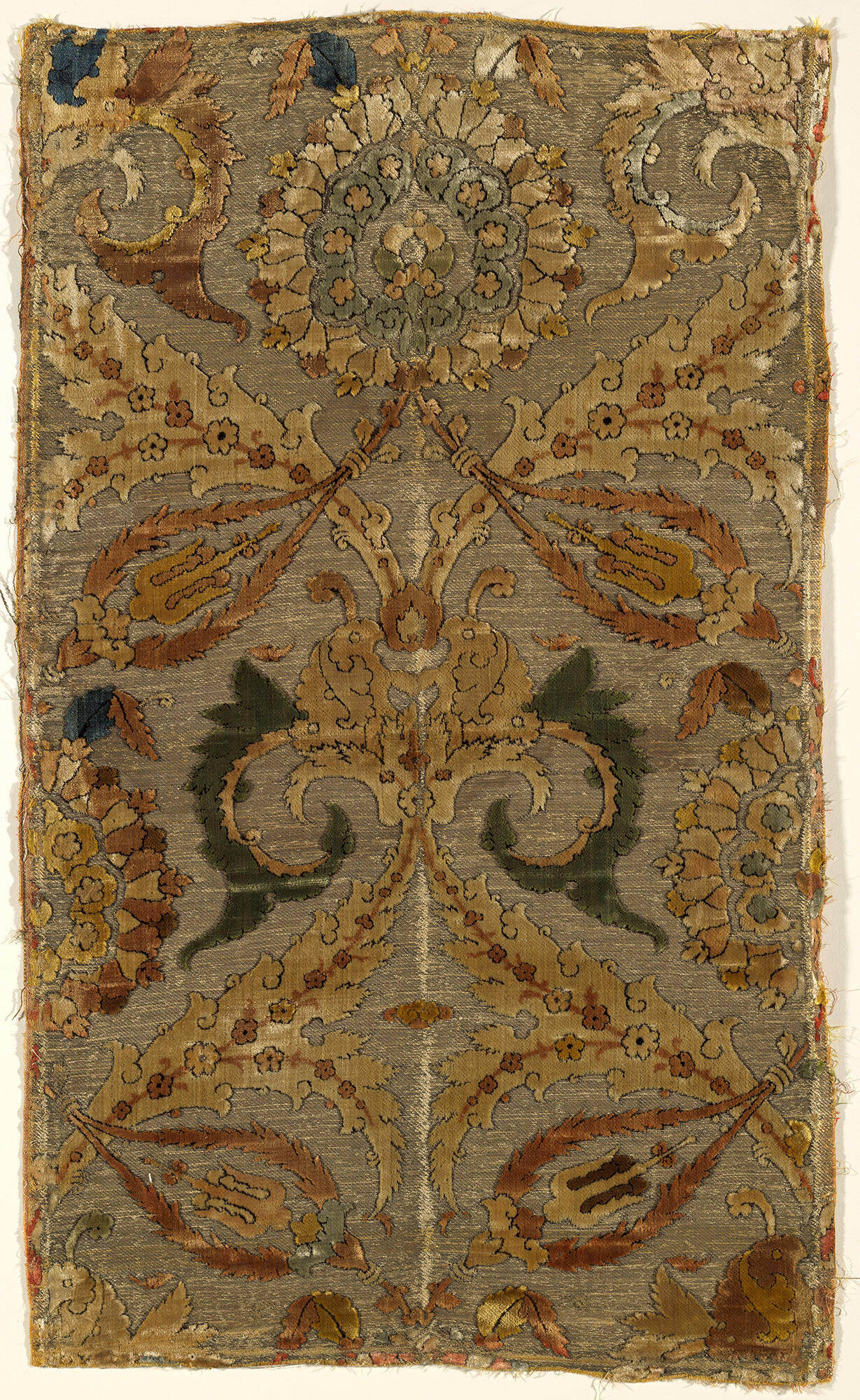 Persian, rectangular, voided velvet with a multicolored cut pile on a tan twill ground faced with gold-colored metallic thread with a stylized floral pattern throughout.