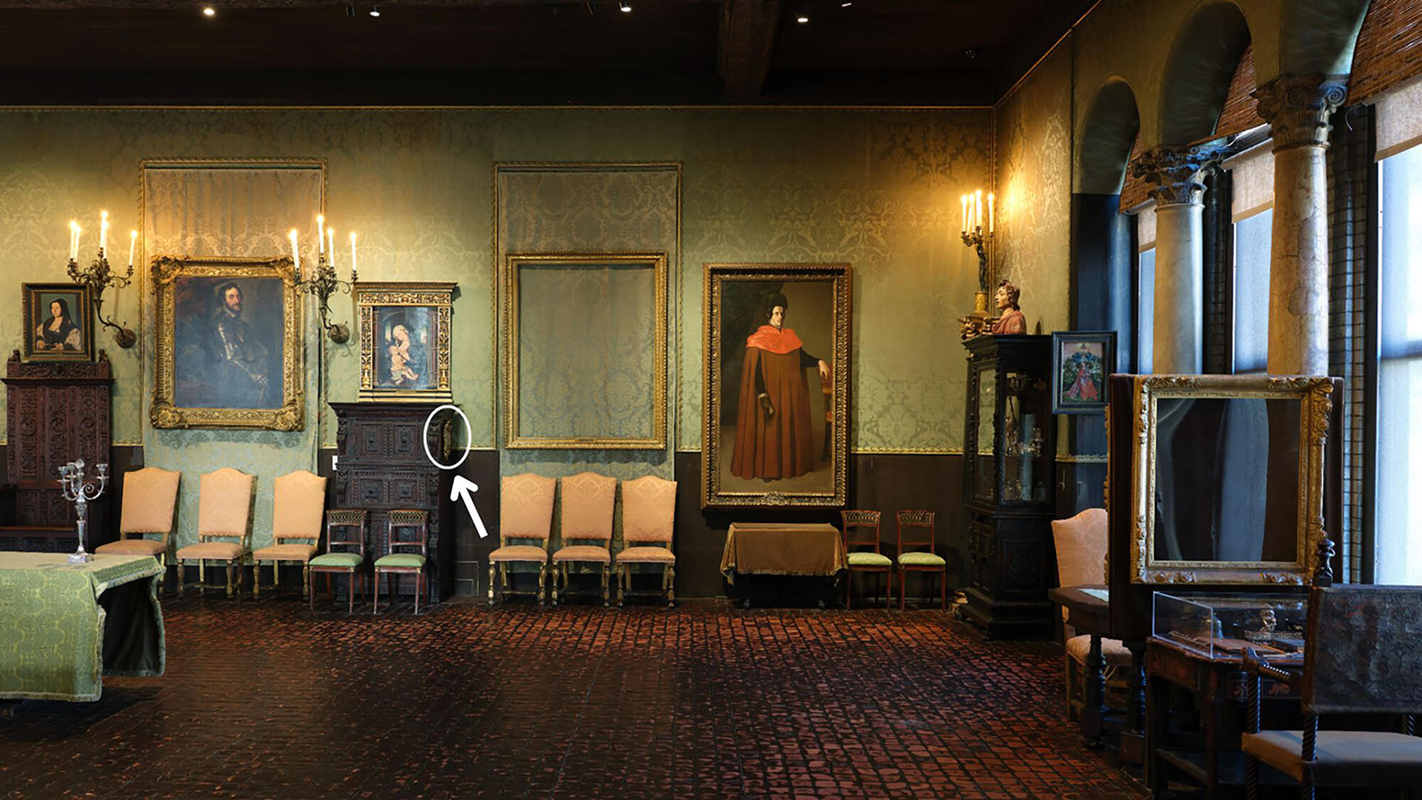 Room with red tiles and green wall textiles lit by reproduction candle sconces, alternating paintings and frames next to chairs and dark wooden furniture including the right side of a walnut cabinet where The Dauphin François D'Angouleme hangs. 