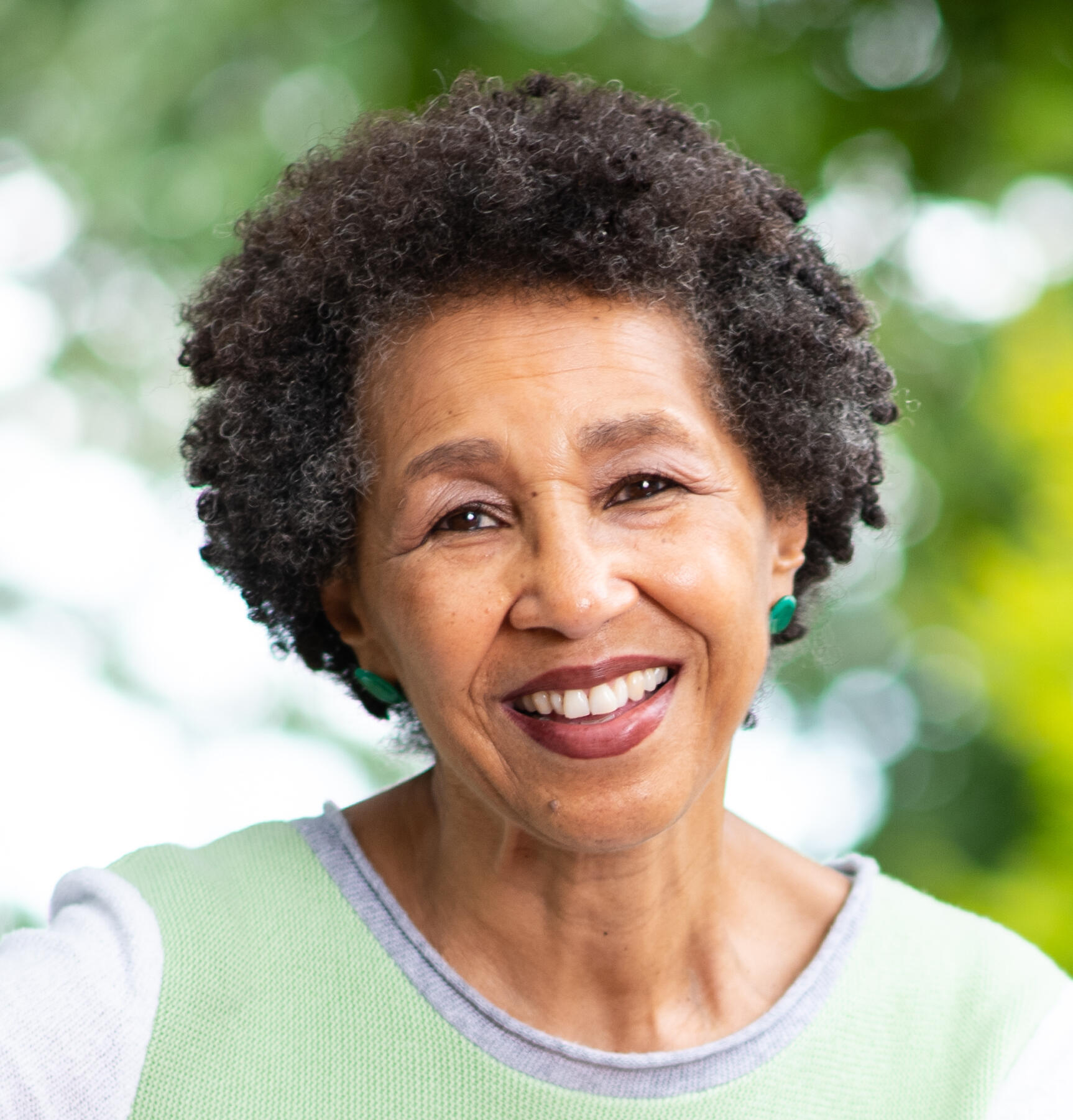 Headshot of a Brown woman with short black hair wearing a pale green top