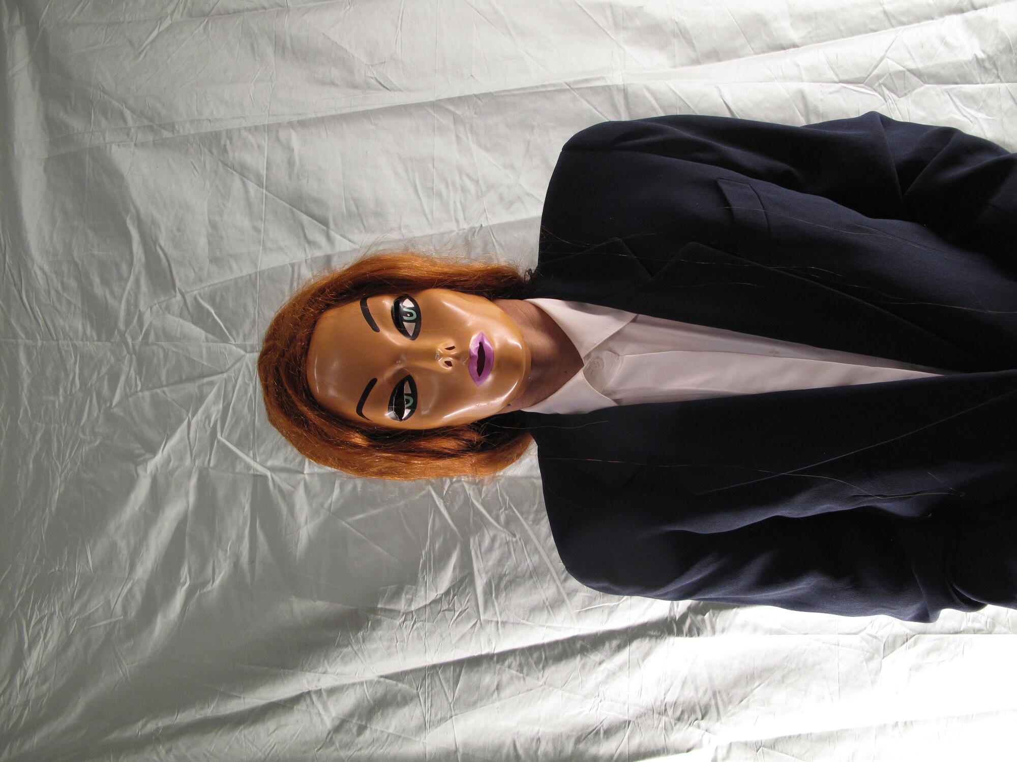 Headshot of a woman in a doll mask wearing a blazer