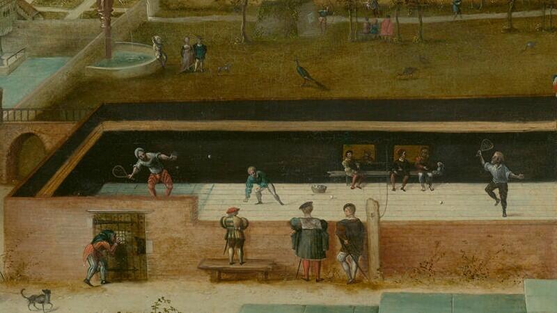An image of an open-air tennis court, surrounded by walls, where two men hold racquets and hit a ball over a rope while spectators look on.