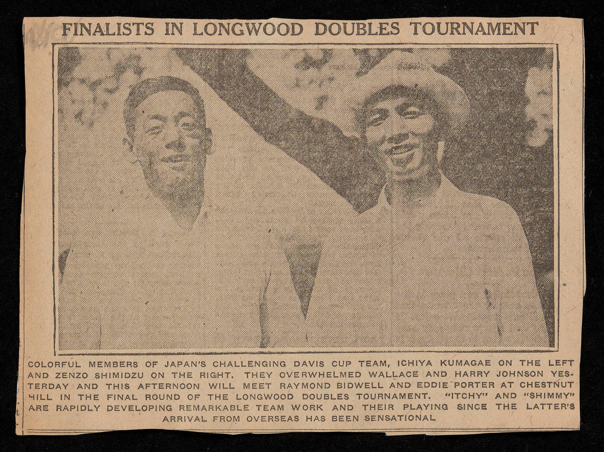 Two men, one wearing a hat, dressed in white shirts. They are photographed from the waist up, and they are smiling at the camera.