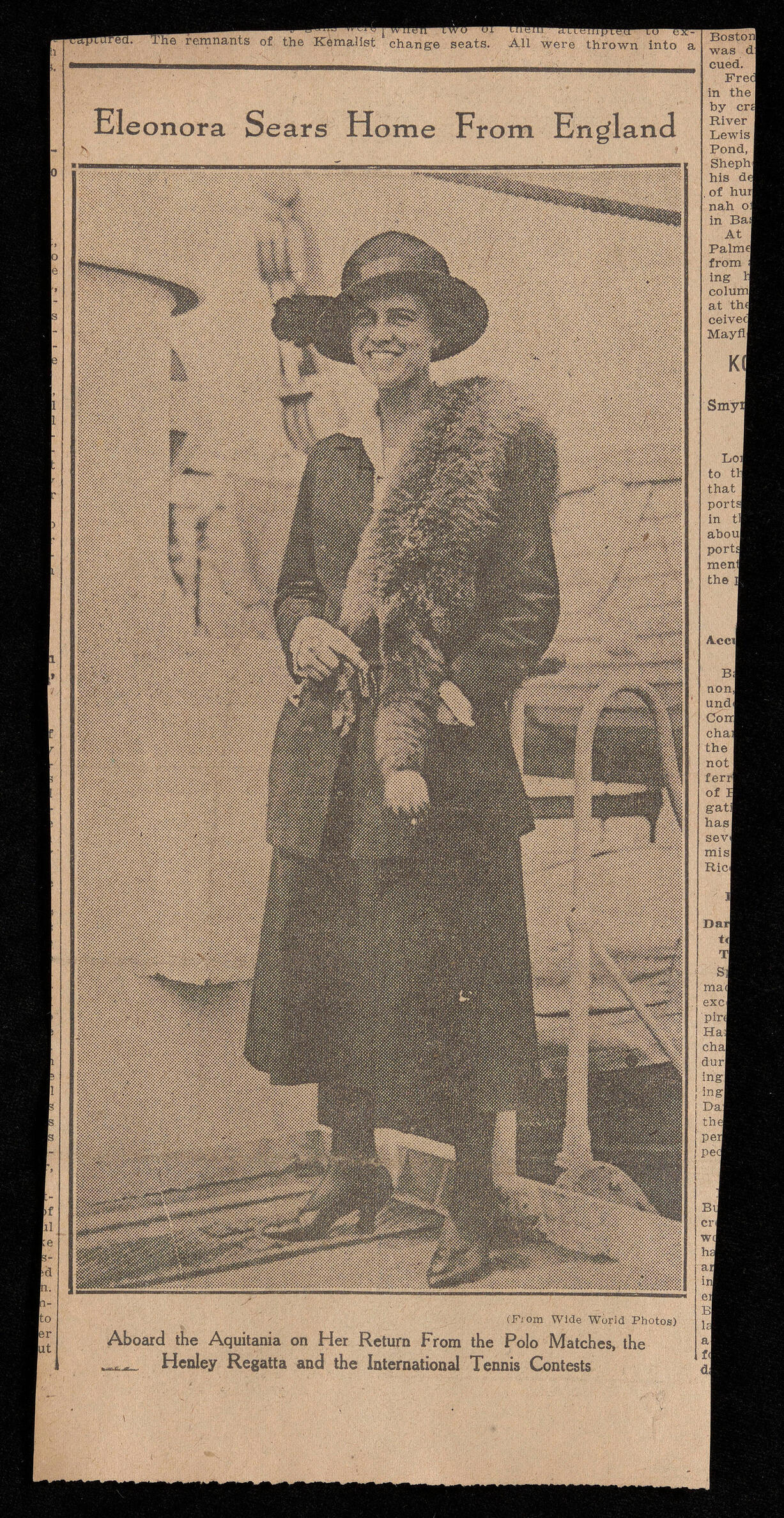 A newspaper clipping of a photograph and caption. The photograph shows a woman standing on the deck of a boat. She is smiling and wearing a hat, a fur stole, and a long skirt.