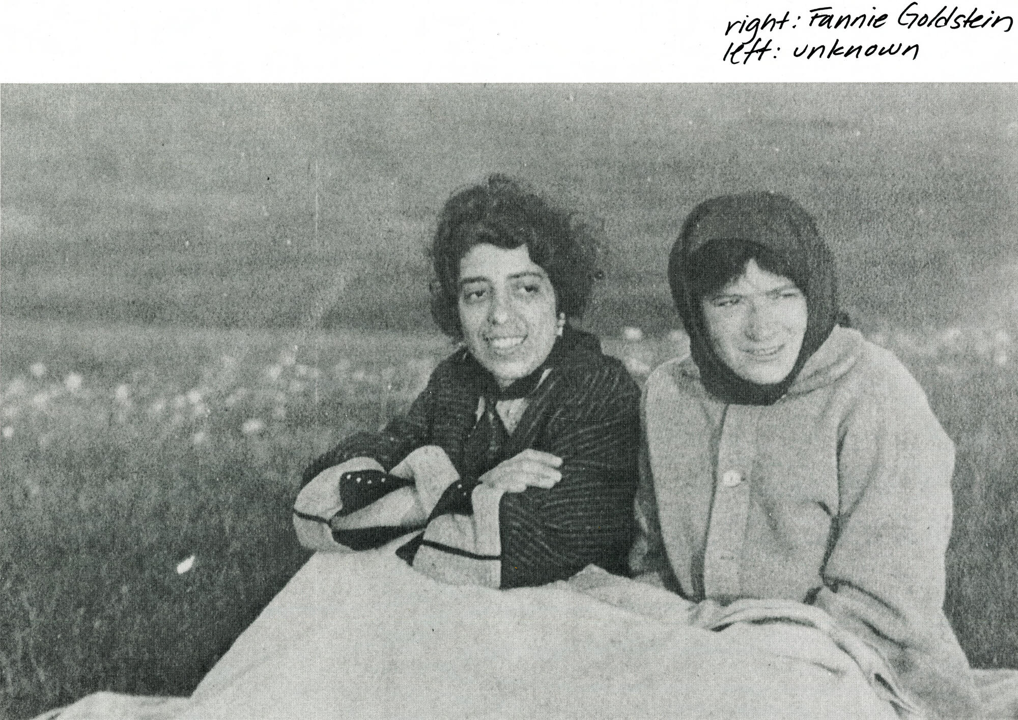 Two young women seated outside with a blanket and wearing coats.