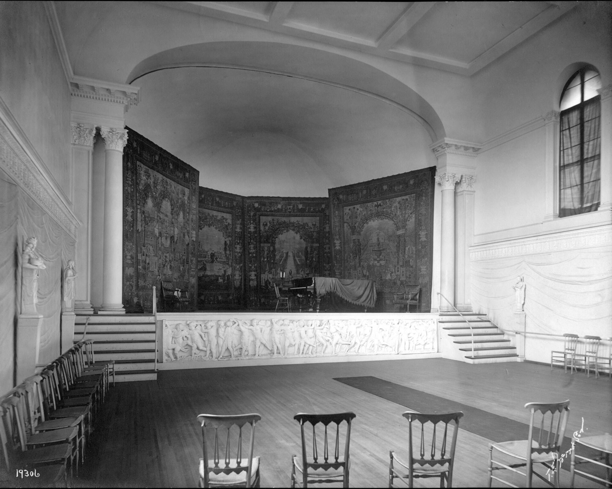 A black and white photograph of a concert hall with a stage that has a series of tapestries hanging on the back wall.