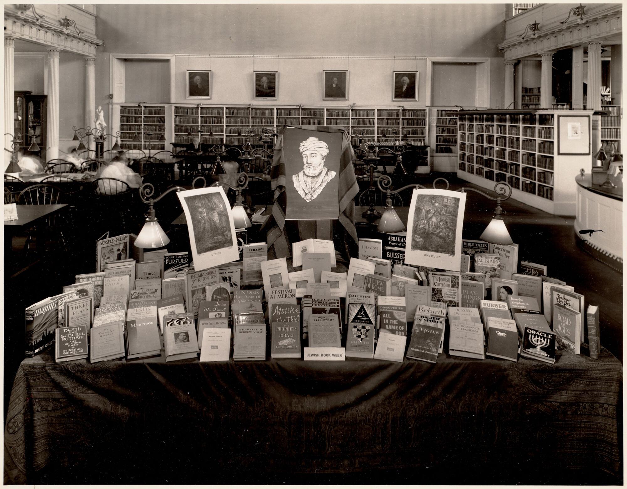 A black and white photograph of a table in a library displaying many books for Jewish book week.