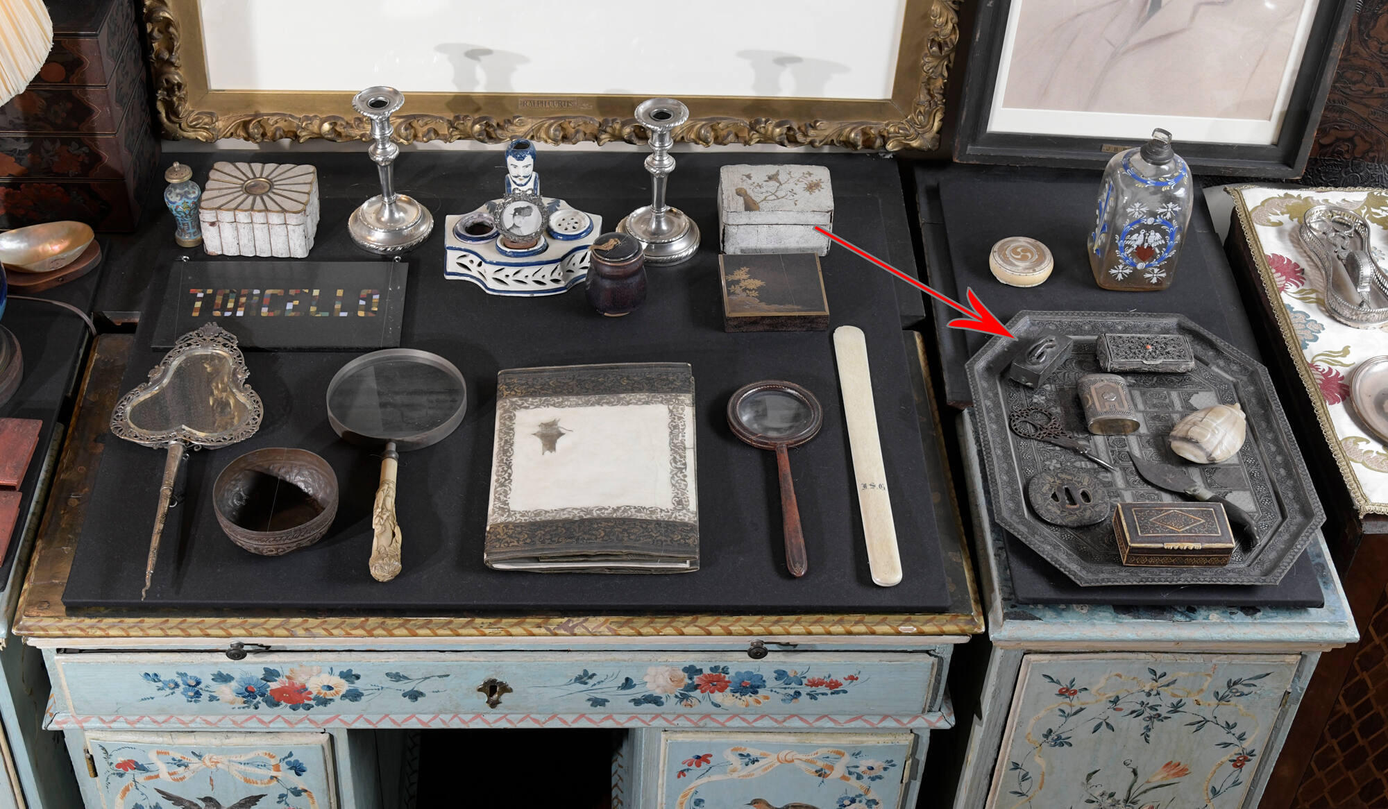 Desk with many small objects on top of it, including a mirror, magnifying glass, candlesticks, and many small containers.