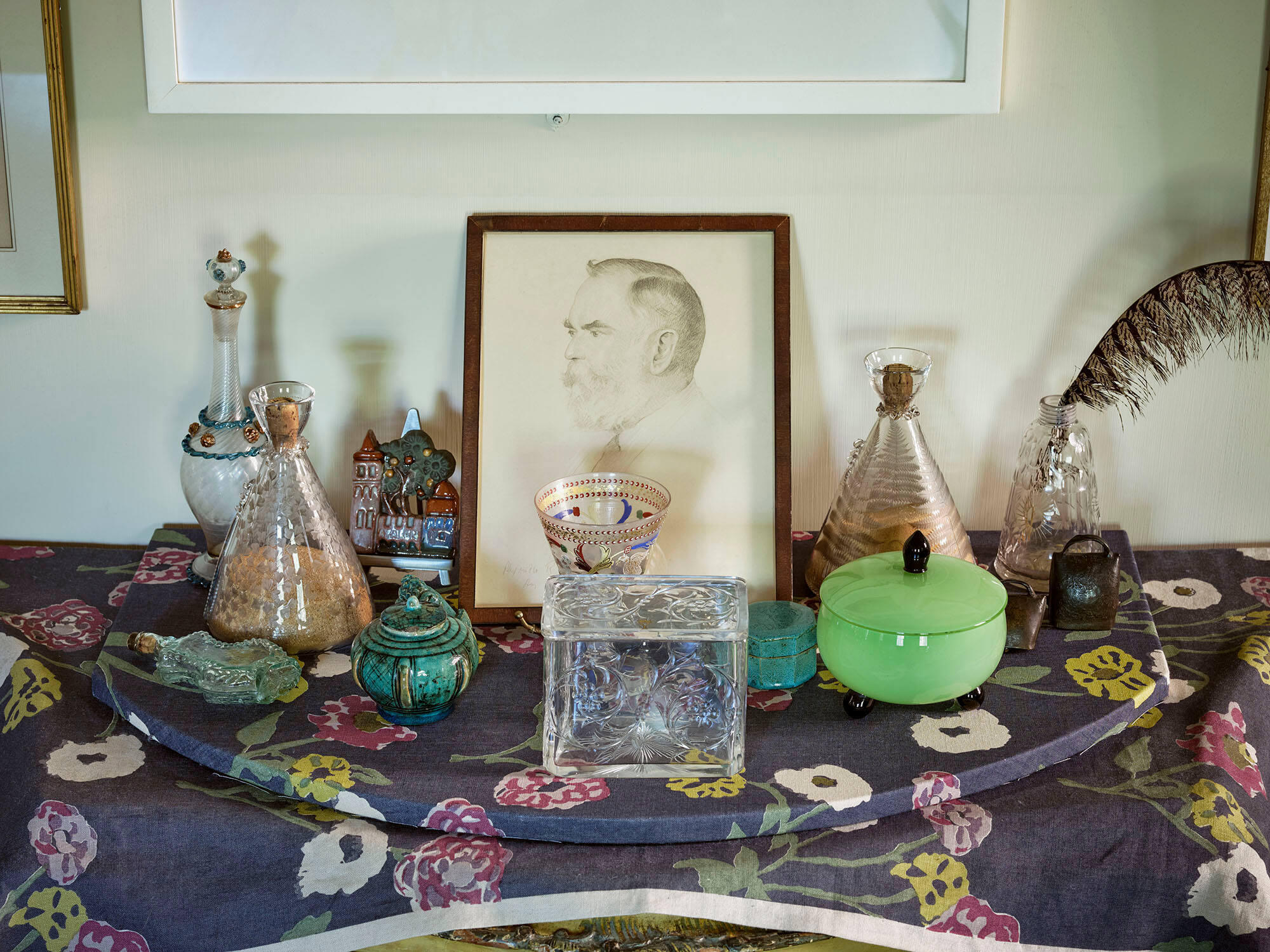 Table covered in objects, including a portrait and many glass and ceramic vessels