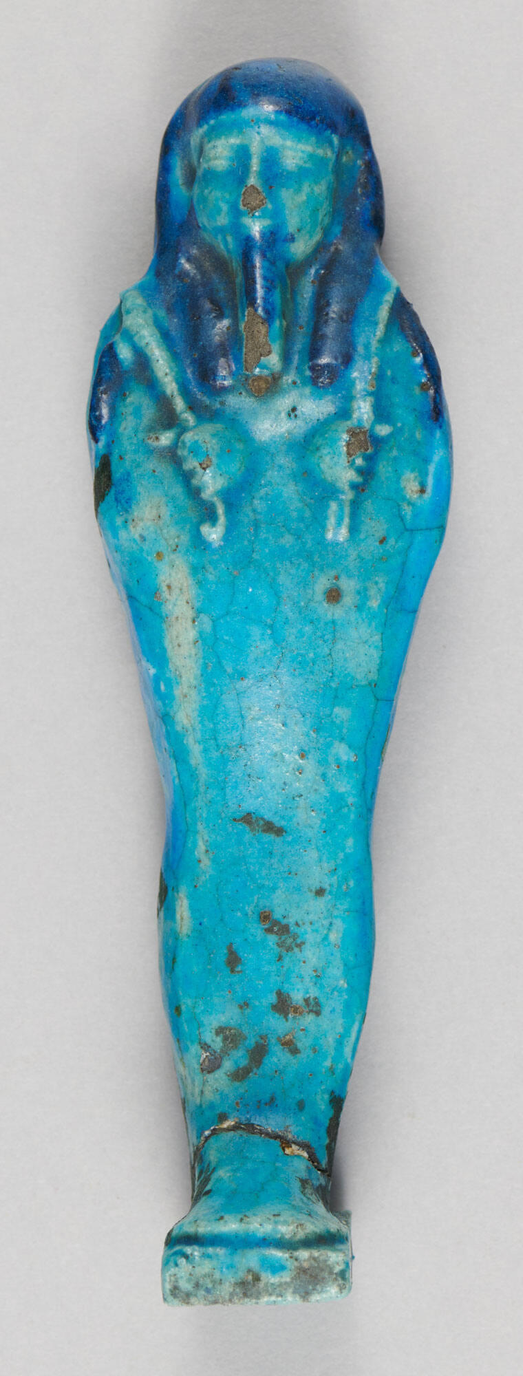 Blue ceramic figure with arms crossed, legs pressed together, and a headcovering.