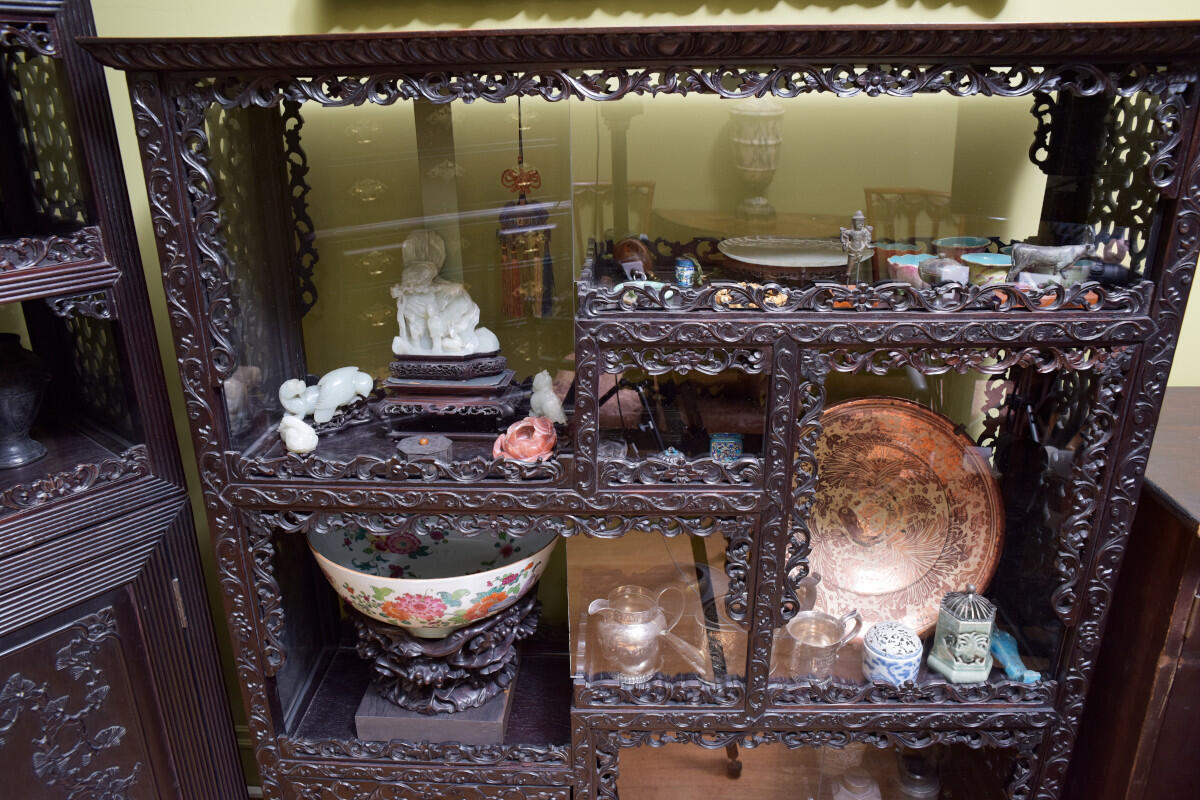 Ornately carved wooden cabinet whose alternating shelves are filled with objects, primarily ceramics.