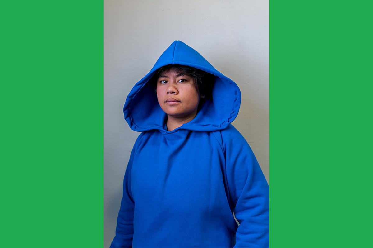 An Urbano Project student shows off their finished Map This garment: a royal blue hoodie with a wide, dramatic hood.