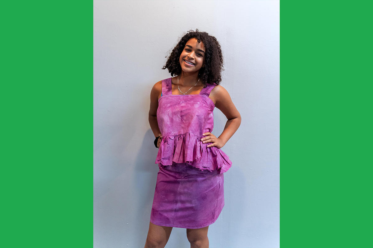 An Urbano Project student shows off their finished Map This garment: a tie-dyed pink top-and-skirt set. The top has a large ruffle at the waist.