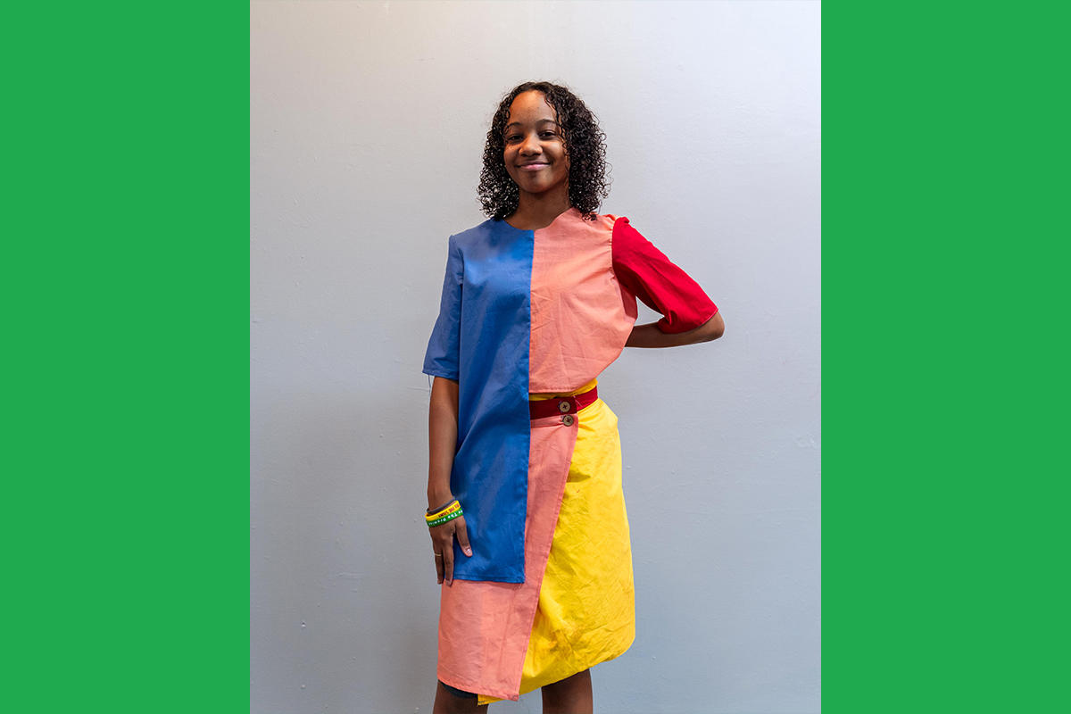 An Urbano Project student shows off their finished Map This garment: a colorblocked top-and-skirt set in bold primary colors..