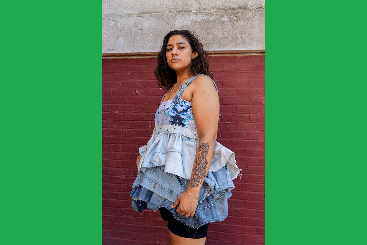 An Urbano Project student shows off their finished Map This garment: a top with large ruffles made of recycled denim in various washes, grading from light wash to medium.