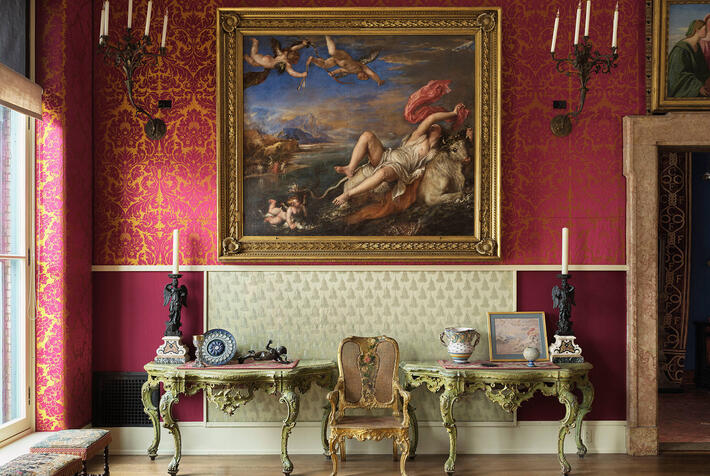 A room with red and yellow upholstered walls filled with paintings.