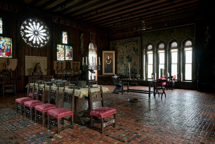 A room with wooden beams, stained glass, decorative tiles with a portrait in the center of the image.